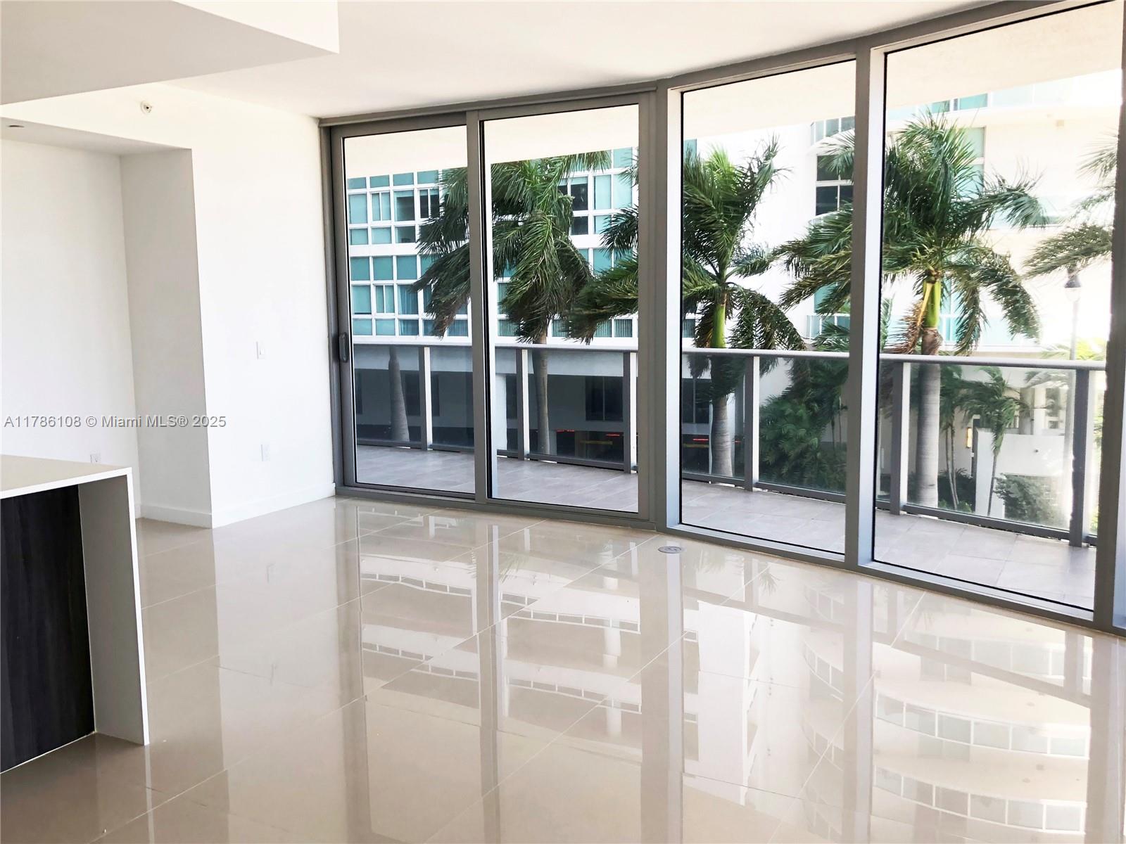 A bright, empty room features glossy tile floors, white walls, and large floor-to-ceiling glass doors — 488 NE 18th St # 215, Miami FL 33132, MIAMI, FL