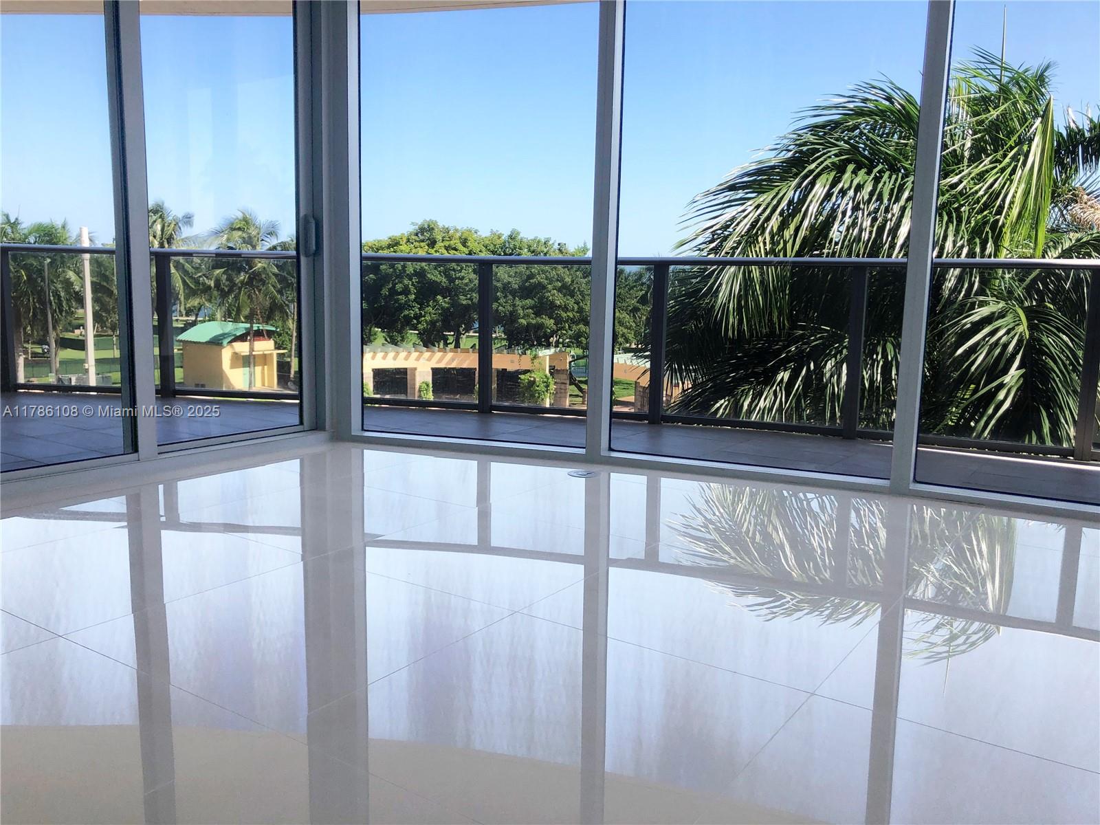 A room with white tile floors and floor-to-ceiling windows overlooking a balcony and trees — 488 NE 18th St # 215, Miami FL 33132, MIAMI, FL