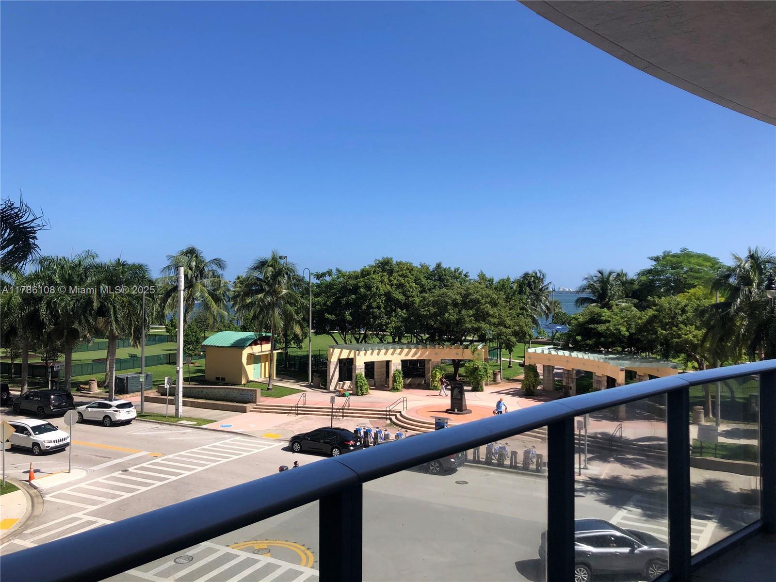 A balcony overlooks a park with palm trees, a pedestrian plaza, and a nearby waterfront — 488 NE 18th St # 215, Miami FL 33132, MIAMI, FL