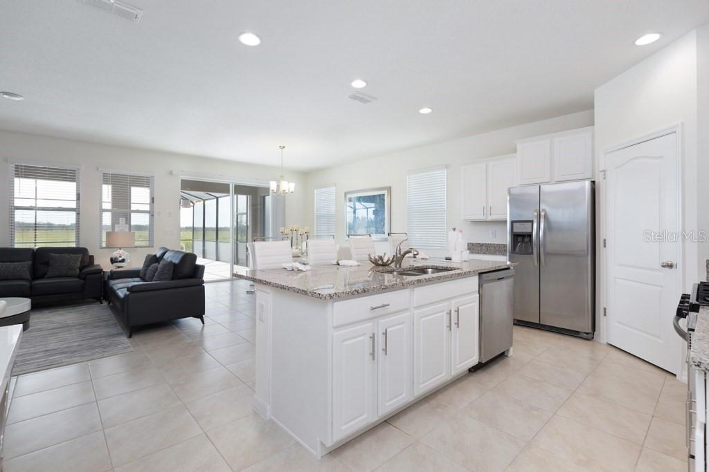 A kitchen with a granite-topped island and white cabinets opens into a living room area — 8012 OAK SHADOW COURT, DAVENPORT, FL