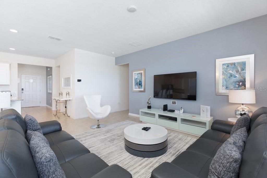 A living room features gray leather sofas, a round coffee table, and a wall-mounted television — 8012 OAK SHADOW COURT, DAVENPORT, FL