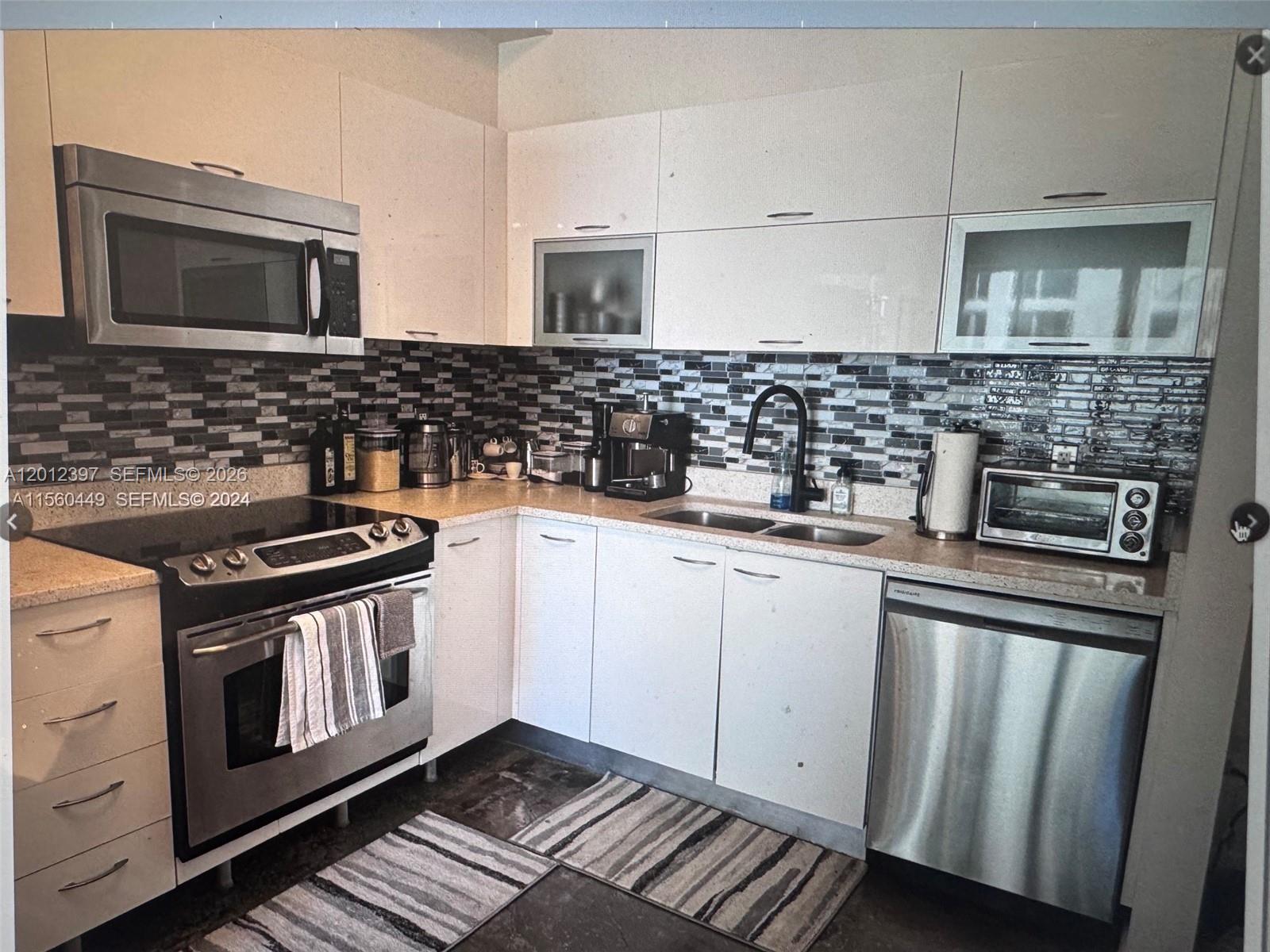 A kitchen features white flat-panel cabinets, stainless steel appliances, and a dark mosaic tile backsplash — 133 NE 2nd Ave # 2003, Miami FL 33132, MIAMI, FL