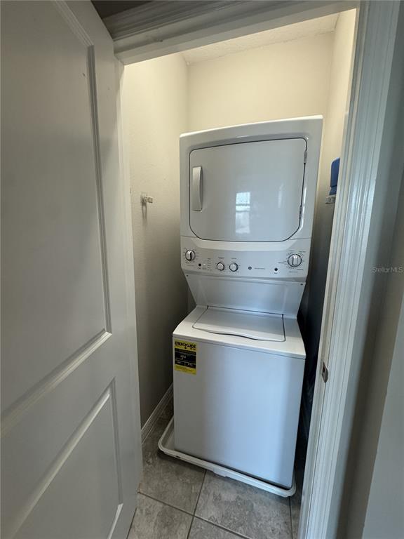 A white stacked washer and dryer unit sits inside a small tiled laundry closet — 16042 MICELLI DRIVE, WINTER GARDEN, FL