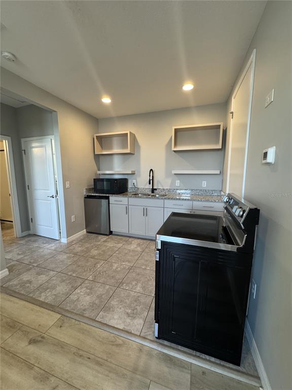 A kitchen features gray cabinets, granite countertops, a black stove, and tile flooring — 16042 MICELLI DRIVE, WINTER GARDEN, FL