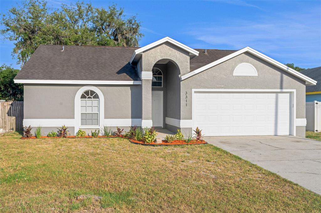 A single-story gray house with a white garage door, arched entryway, and a grassy lawn — 3311 QUEENS COVE LOOP, WINTER HAVEN, FL