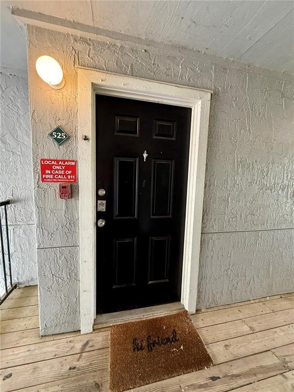 A black front door with a welcome mat and a fire alarm sign on the wall — 3705 SW 27TH STREET UNIT 525, GAINESVILLE, FL
