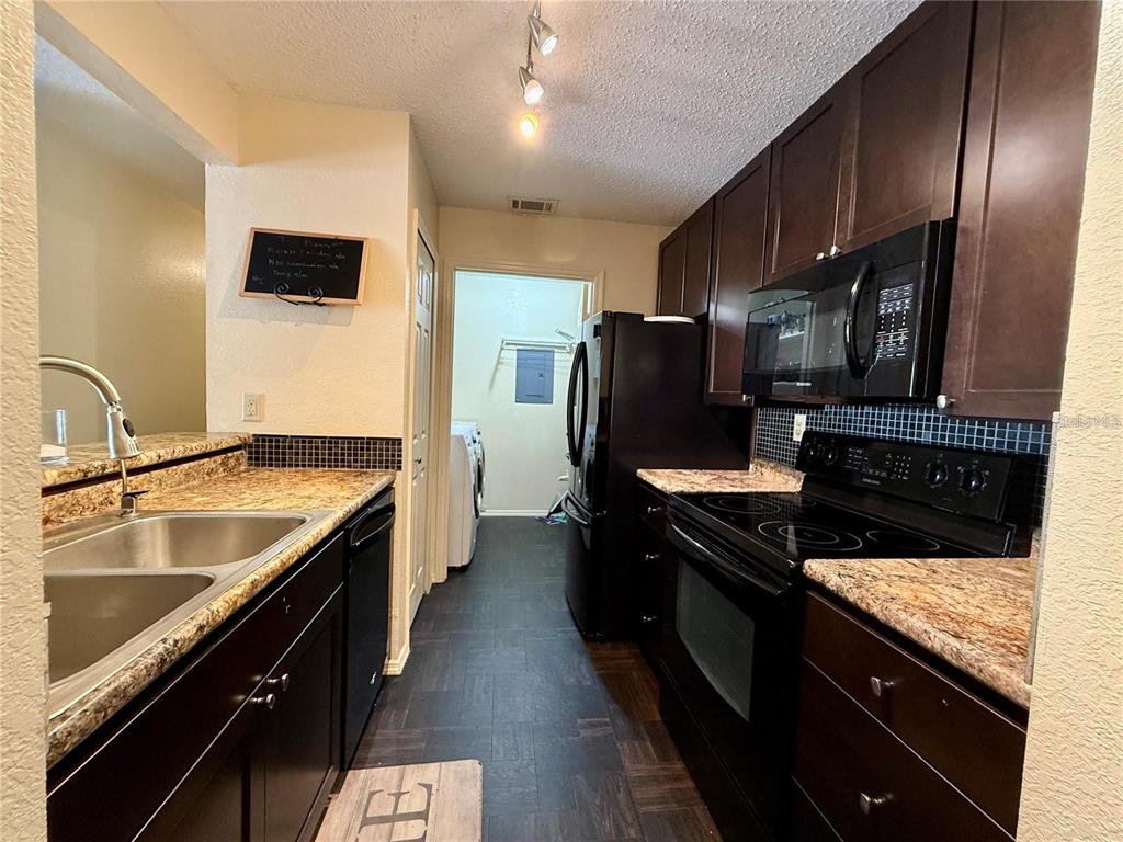 A galley kitchen features dark wood cabinets, granite countertops, black appliances, and a laundry area — 3705 SW 27TH STREET UNIT 525, GAINESVILLE, FL