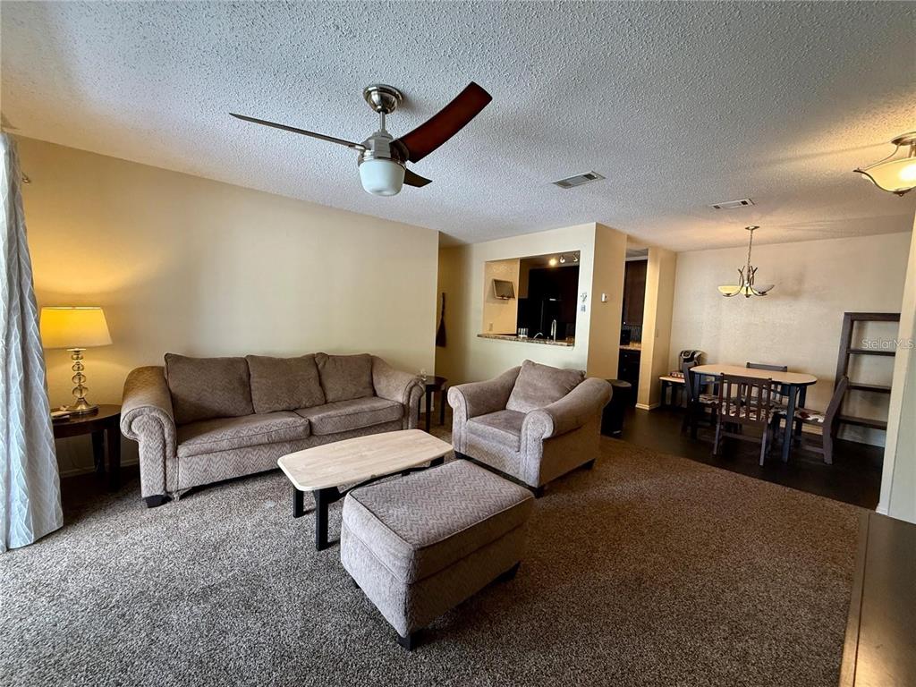 A living room with carpeted floors, a sofa, an armchair, and an adjacent dining area — 3705 SW 27TH STREET UNIT 525, GAINESVILLE, FL