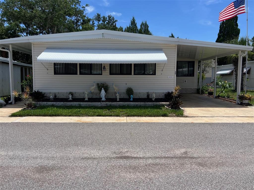 A single-story manufactured home features light siding, a metal awning, and a paved carport — 29250 US HIGHWAY 19 N UNIT 12, CLEARWATER, FL