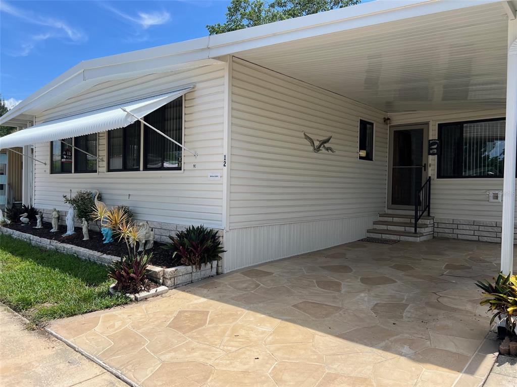 A single-story mobile home with light siding, a stone-paved carport, and a small garden bed — 29250 US HIGHWAY 19 N UNIT 12, CLEARWATER, FL