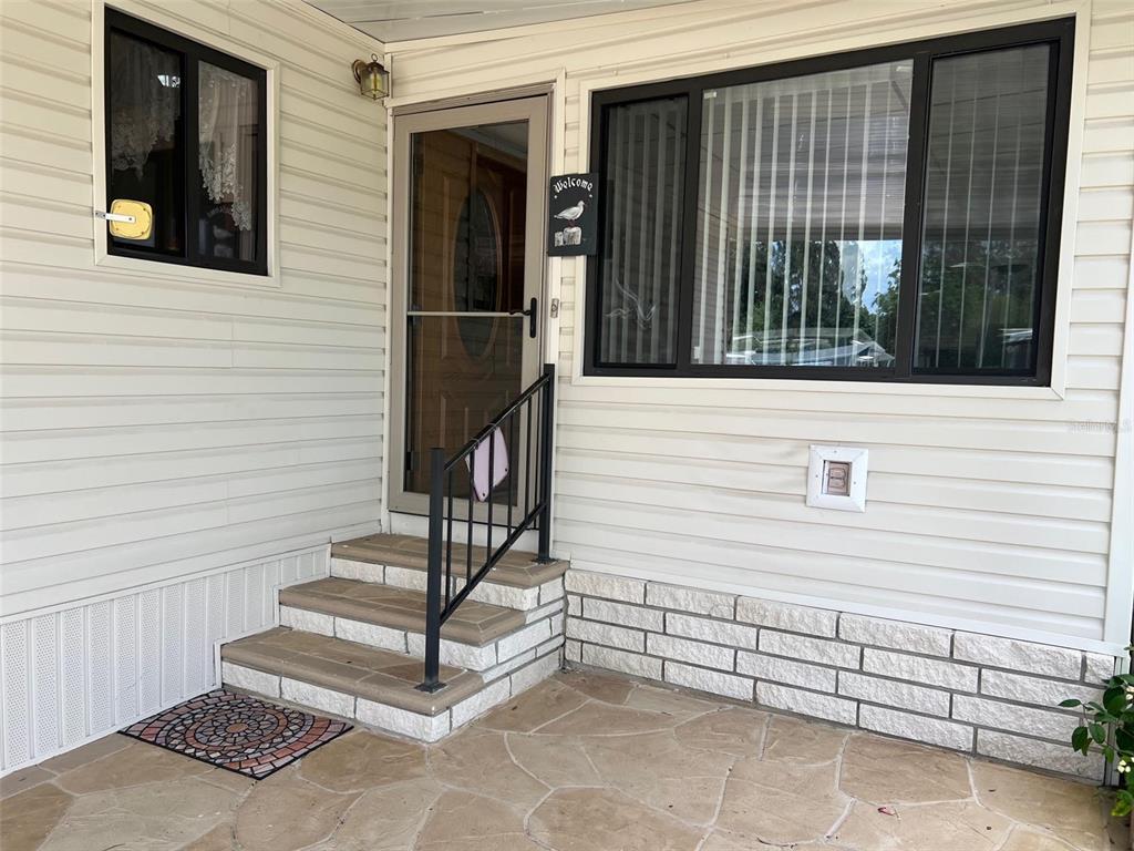 The exterior of a home features light siding, stone accents, a small porch, and steps — 29250 US HIGHWAY 19 N UNIT 12, CLEARWATER, FL
