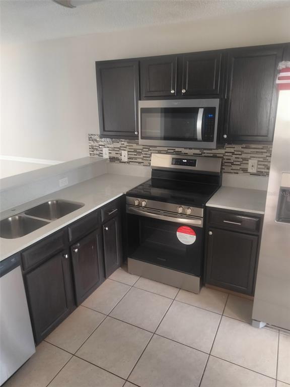 A kitchen features dark wood cabinets, stainless steel appliances, and a tiled backsplash — 6730 BRITTANY CHASE COURT, ORLANDO, FL