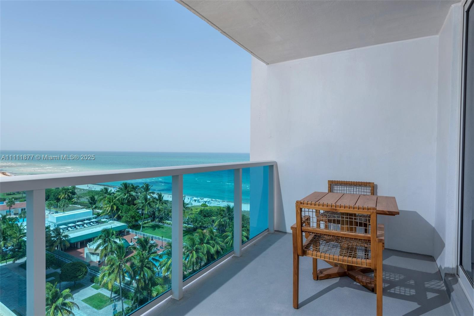 A balcony with a wooden table and chairs overlooks the ocean and palm trees — 102 24th St # 915, Miami Beach FL 33139, MIAMI BEACH, FL