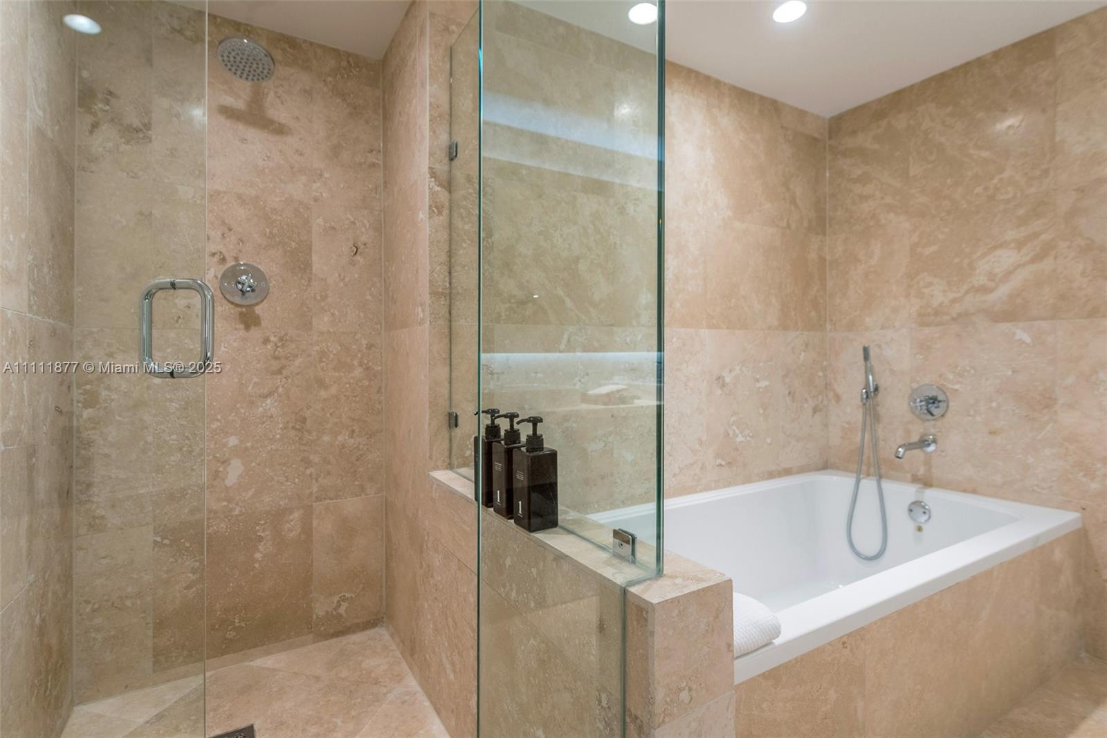A bathroom features a glass-enclosed walk-in shower and a separate bathtub with beige stone tiling — 102 24th St # 915, Miami Beach FL 33139, MIAMI BEACH, FL