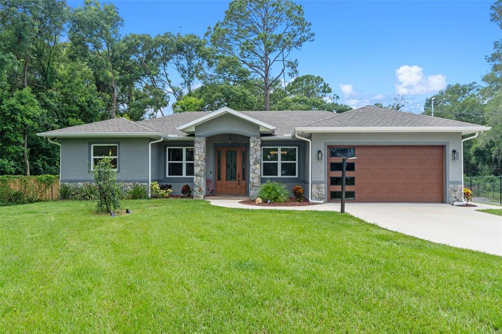 A single-story gray house with stone accents, a wooden front door, and a two-car garage — 308 CHURCH STREET, LAKE HELEN, FL