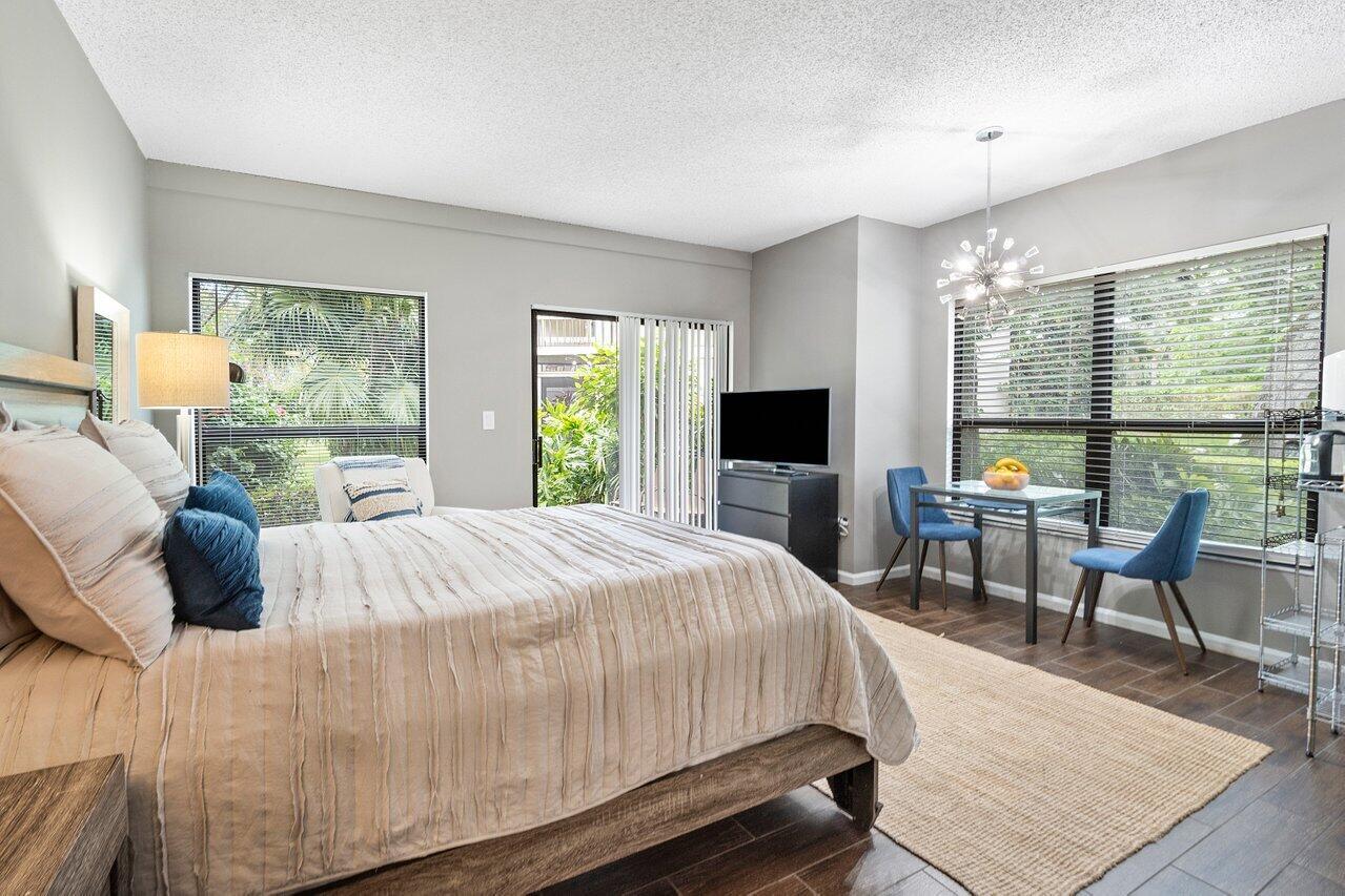 A bedroom features a bed, a small dining table with two chairs, and large windows — 11863 Wimbledon Circle # 407, Wellington FL 33414, WELLINGTON, FL