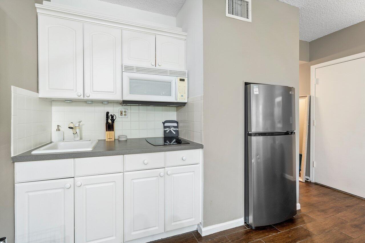 A small kitchen features white cabinets, a stainless steel refrigerator, and a dark countertop — 11863 Wimbledon Circle # 407, Wellington FL 33414, WELLINGTON, FL