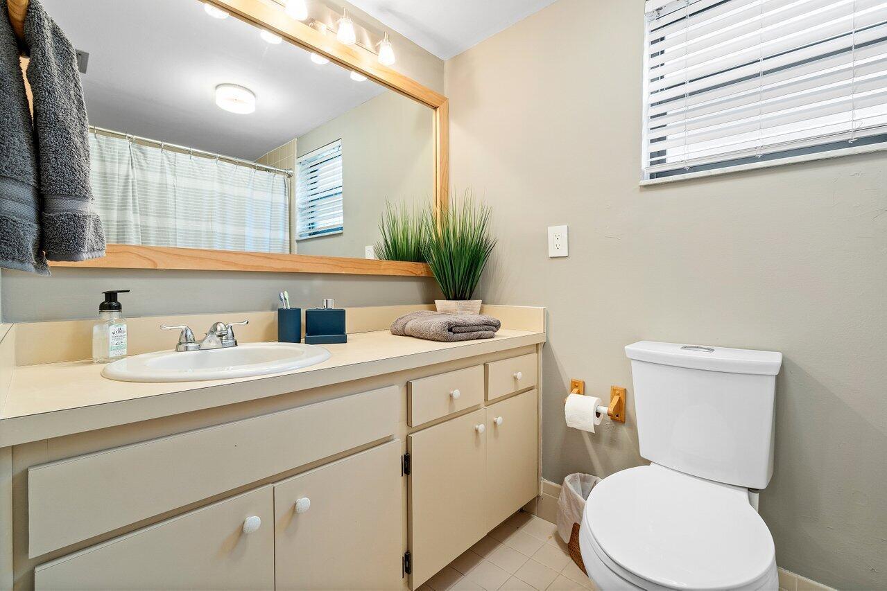 A bathroom features a wood-framed mirror, a beige vanity with a sink, and a toilet — 11863 Wimbledon Circle # 407, Wellington FL 33414, WELLINGTON, FL