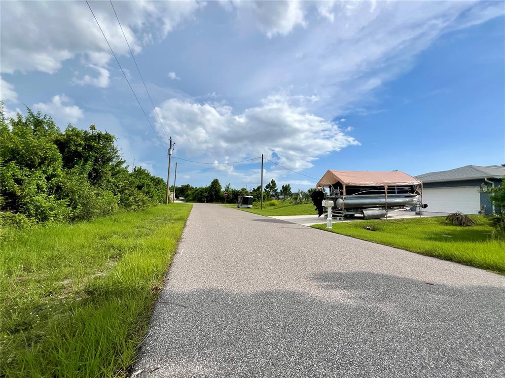 A paved residential street leads toward a house with a boat parked under a canopy — 5602 EYERLY TERRACE, PORT CHARLOTTE, FL