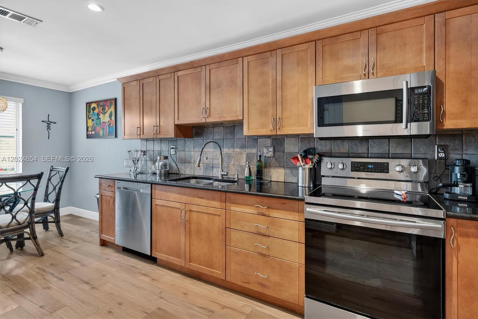 A kitchen features wood cabinets, black countertops, stainless steel appliances, and a tiled backsplash — 14930 SW 104th St # 27, Miami FL 33196, MIAMI, FL