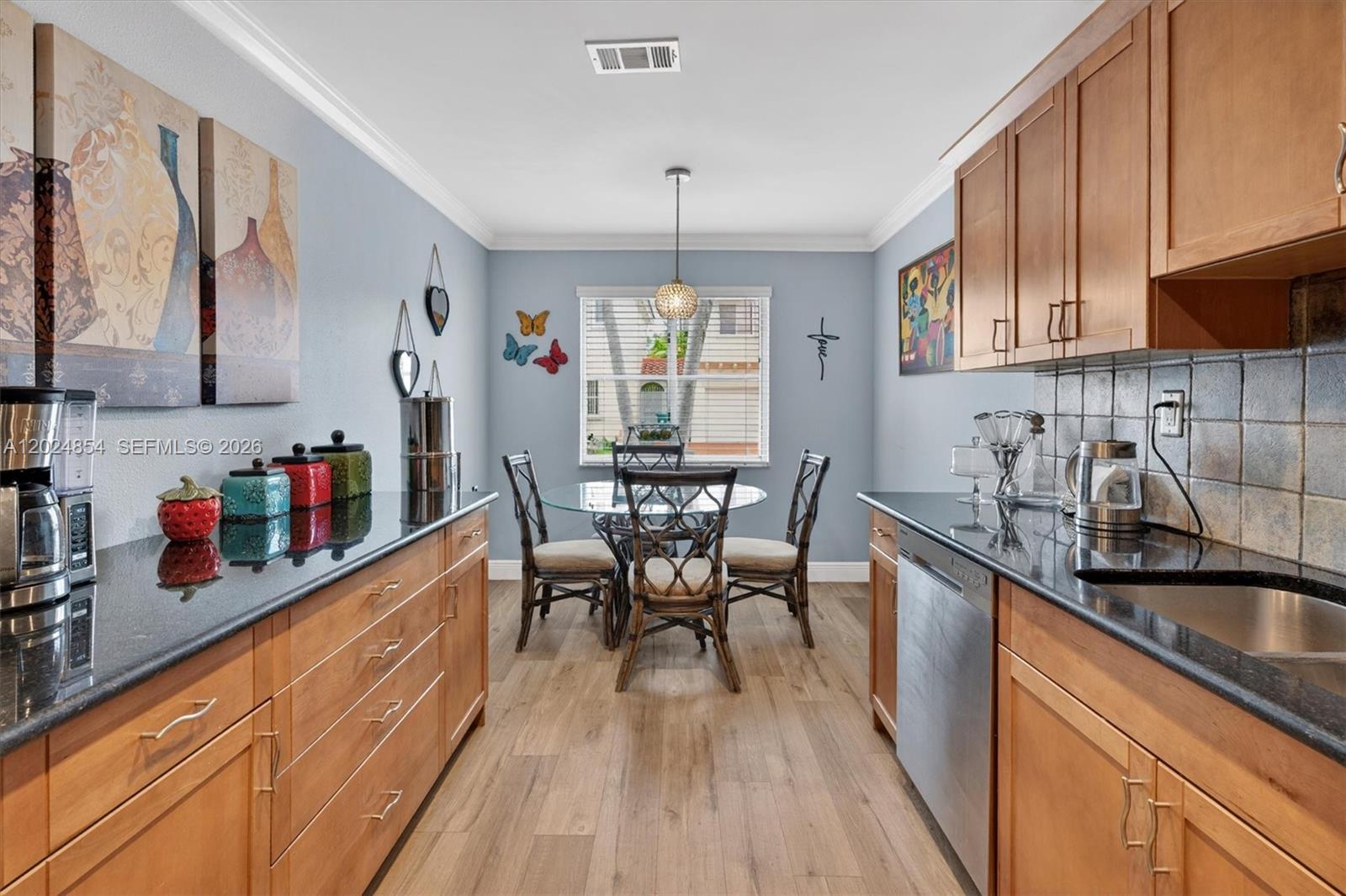 A kitchen with wood cabinets, black countertops, and a dining area with a glass table — 14930 SW 104th St # 27, Miami FL 33196, MIAMI, FL