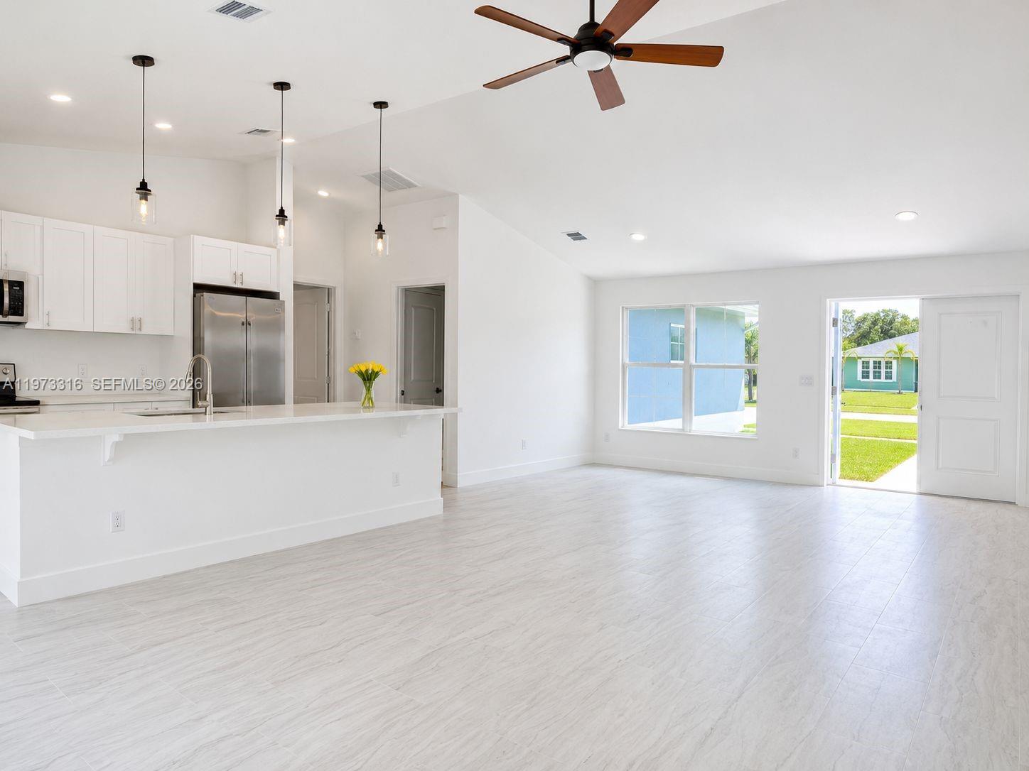 An open-concept living and dining area features light tile floors, a kitchen island, and vaulted ceilings — 9165 100th Ct, Vero Beach FL 32967, VERO BEACH, FL