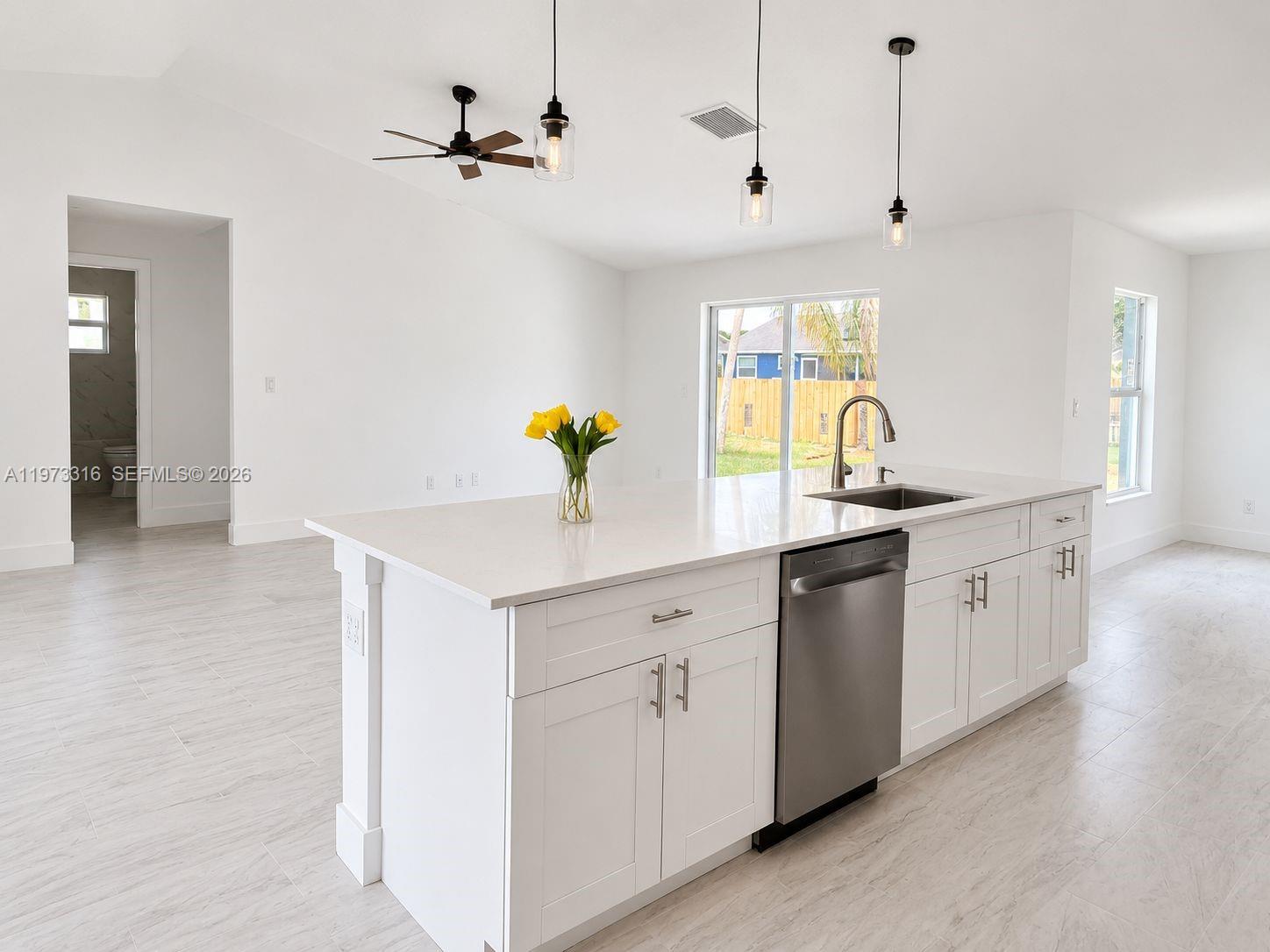 A kitchen island with a sink and pendant lighting sits in a bright, open-concept room — 9165 100th Ct, Vero Beach FL 32967, VERO BEACH, FL