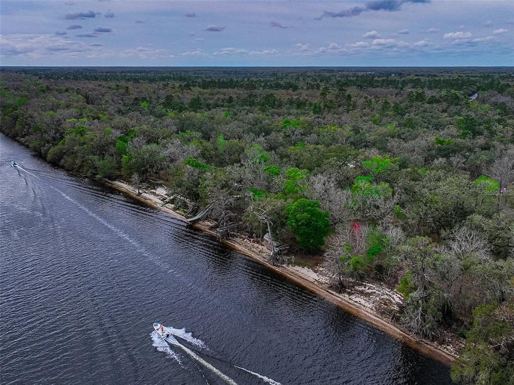 An aerial view shows a motorboat traveling along a river beside a wooded shoreline — 2878 NE 340 HIGHWAY, BRANFORD, FL