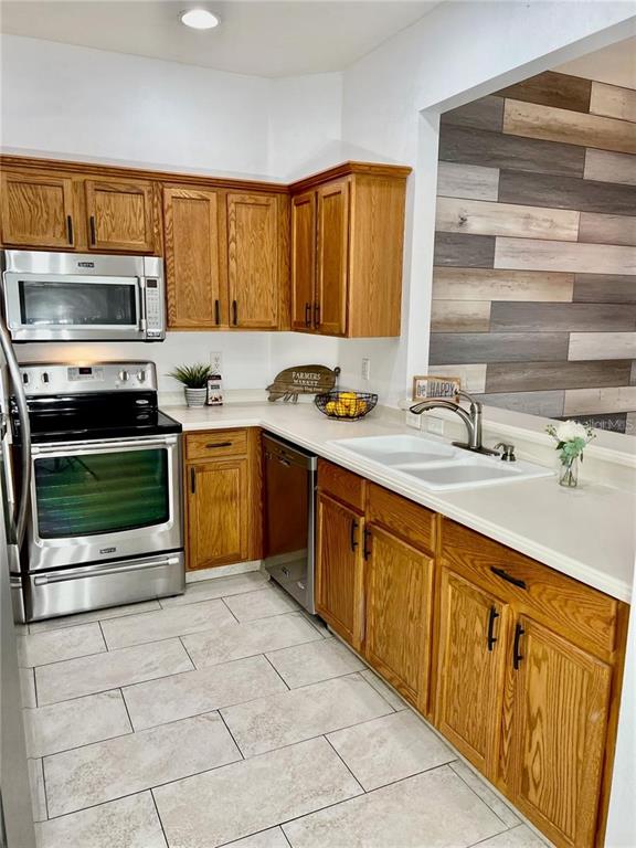 A kitchen features oak cabinets, stainless steel appliances, white countertops, and a wood-plank accent wall — 3762 PARKRIDGE CIRCLE UNIT 23-106, SARASOTA, FL