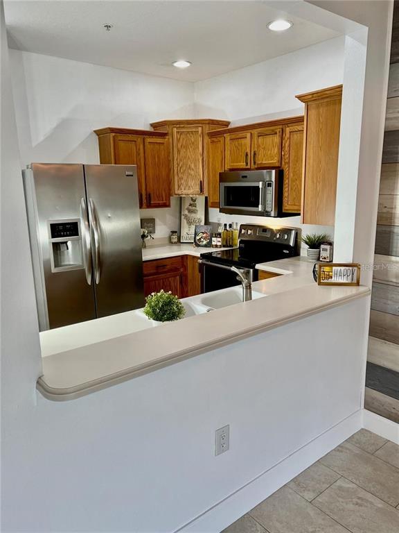 A kitchen features wood cabinets, stainless steel appliances, and a white countertop breakfast bar — 3762 PARKRIDGE CIRCLE UNIT 23-106, SARASOTA, FL