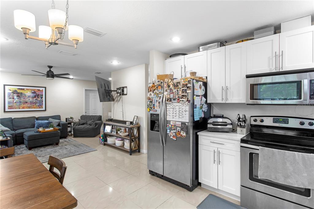A kitchen with white cabinets and stainless steel appliances opens into a living room area — 4215 W BAY VISTA AVENUE, TAMPA, FL