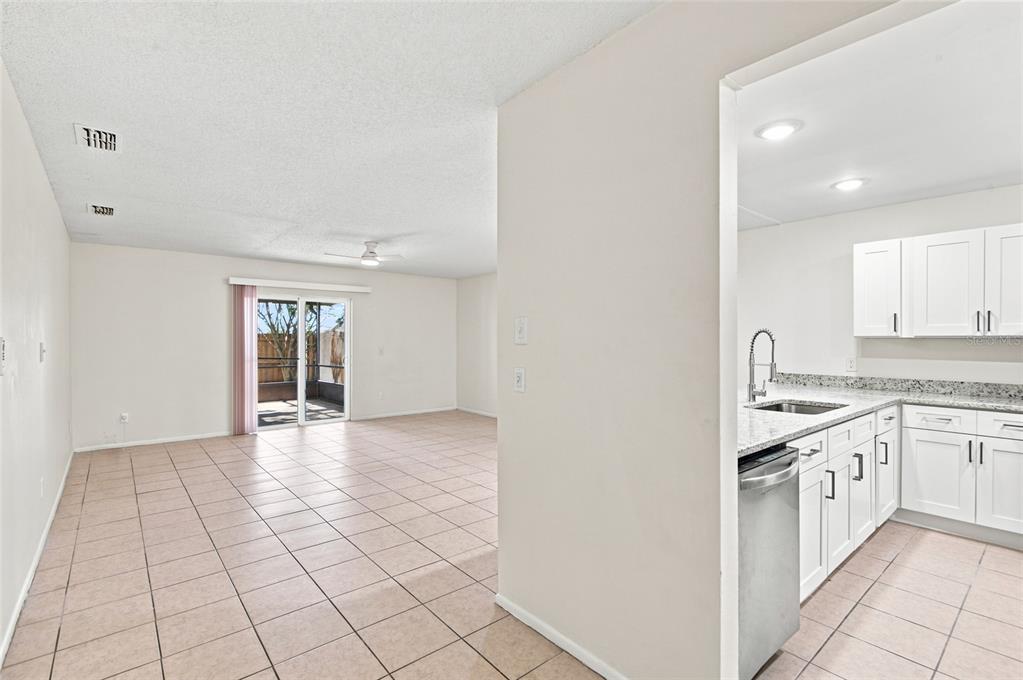 A view from a kitchen with white cabinets and granite countertops looking into a living area — 5967 FISH COURT, ORLANDO, FL