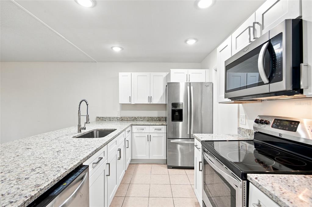 A kitchen with white cabinets, granite countertops, stainless steel appliances, and tile flooring — 5967 FISH COURT, ORLANDO, FL