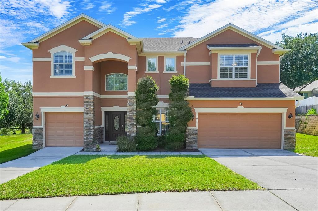 A two-story suburban house with a tan stucco exterior, stone accents, and a three-car garage — 11045 LEMAY DRIVE, CLERMONT, FL
