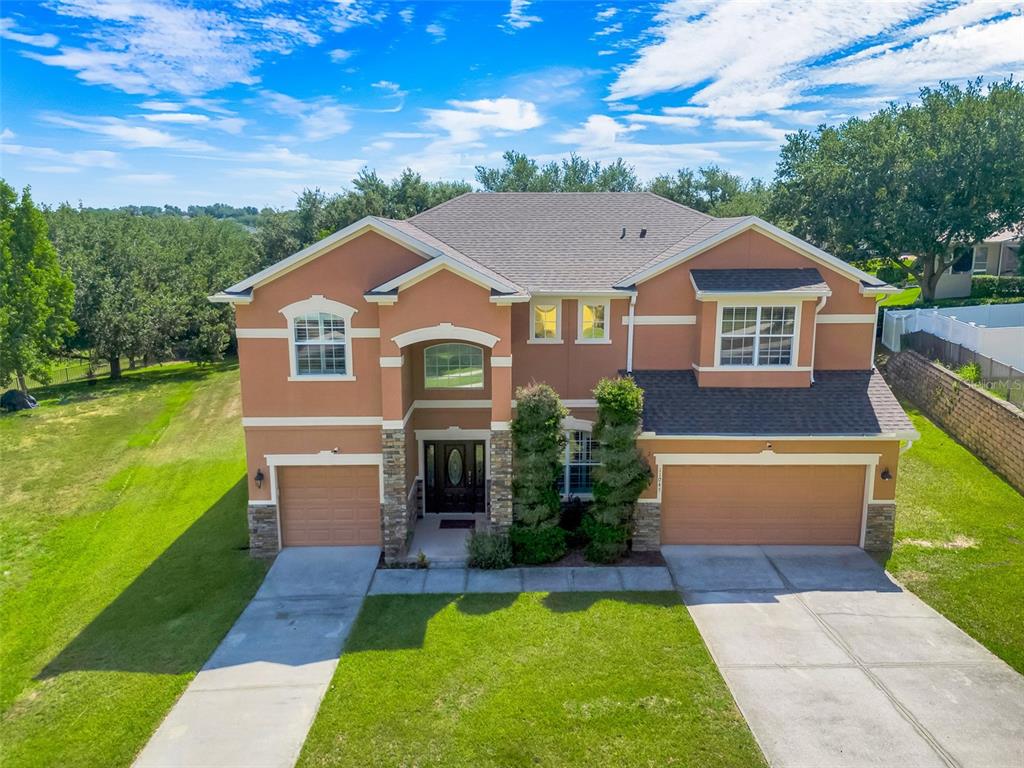 A two-story stucco house features two garage doors, a stone-accented entryway, and a grassy yard — 11045 LEMAY DRIVE, CLERMONT, FL