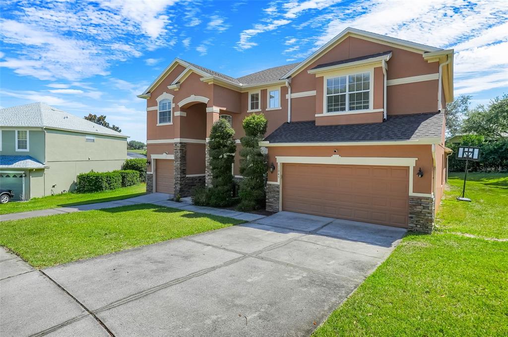 A two-story house with a tan stucco exterior, stone accents, and a three-car garage — 11045 LEMAY DRIVE, CLERMONT, FL