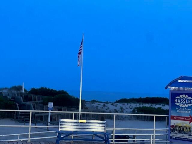 A bench sits on a wooden boardwalk near a beach ramp with an American flag — 1904 Boardwalk, NJ, NJ