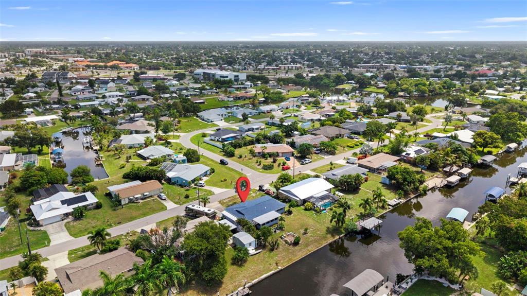 An aerial view shows a residential house with a blue roof situated along a canal — 115 BEDFORD DRIVE NE, PORT CHARLOTTE, FL