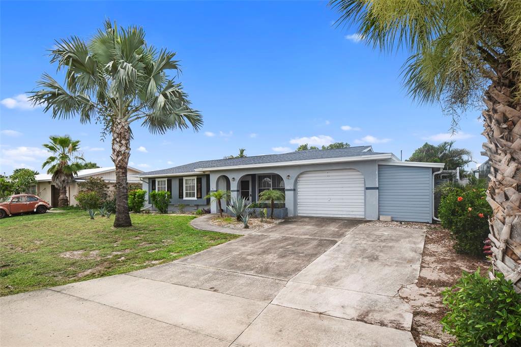 A single-story house with a gray exterior, a front garage, and a palm tree-lined lawn — 115 BEDFORD DRIVE NE, PORT CHARLOTTE, FL