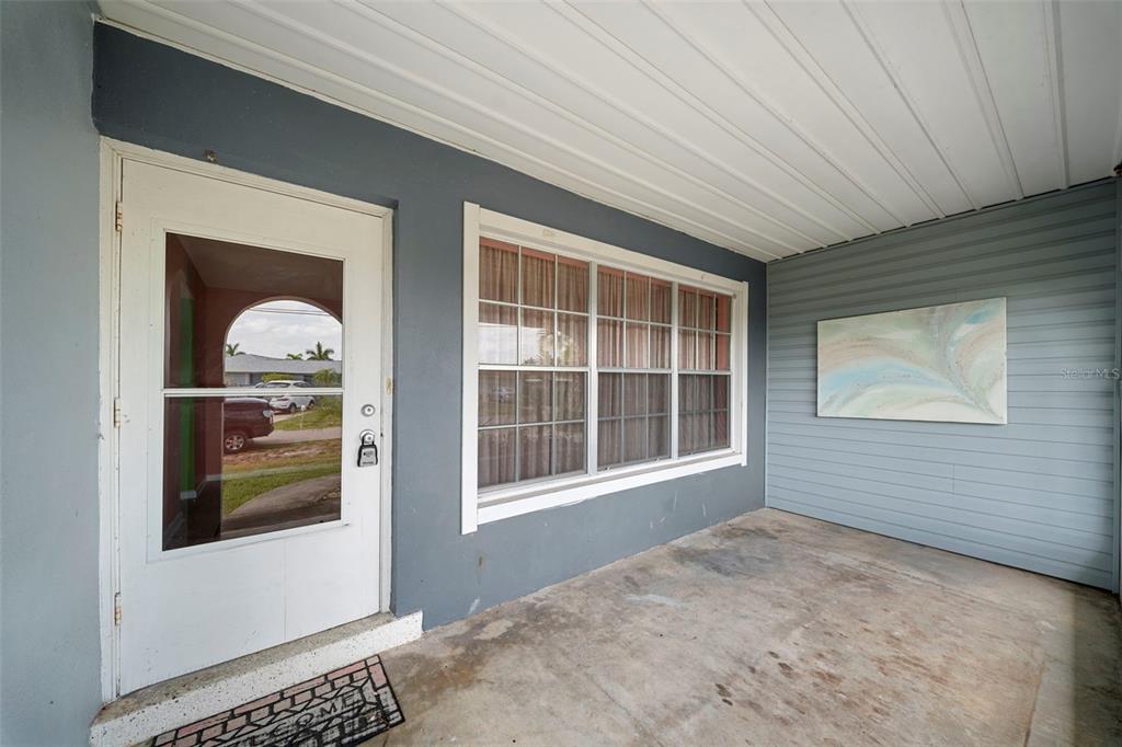 A covered porch features a white storm door, a large window, and light blue siding — 115 BEDFORD DRIVE NE, PORT CHARLOTTE, FL