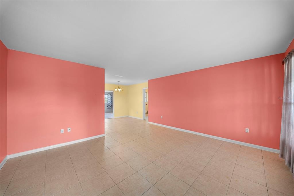 An interior view shows a living room with peach walls, tile flooring, and a yellow dining area — 115 BEDFORD DRIVE NE, PORT CHARLOTTE, FL