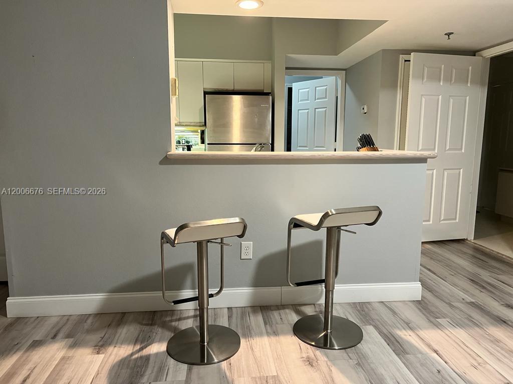 A kitchen pass-through window overlooks a dining area with two bar stools on wood-look flooring — AVENTURA, FL