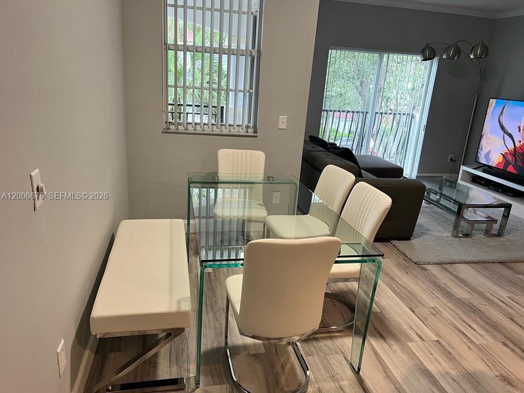 A dining area features a glass table, white chairs, and a bench on wood-look flooring — AVENTURA, FL