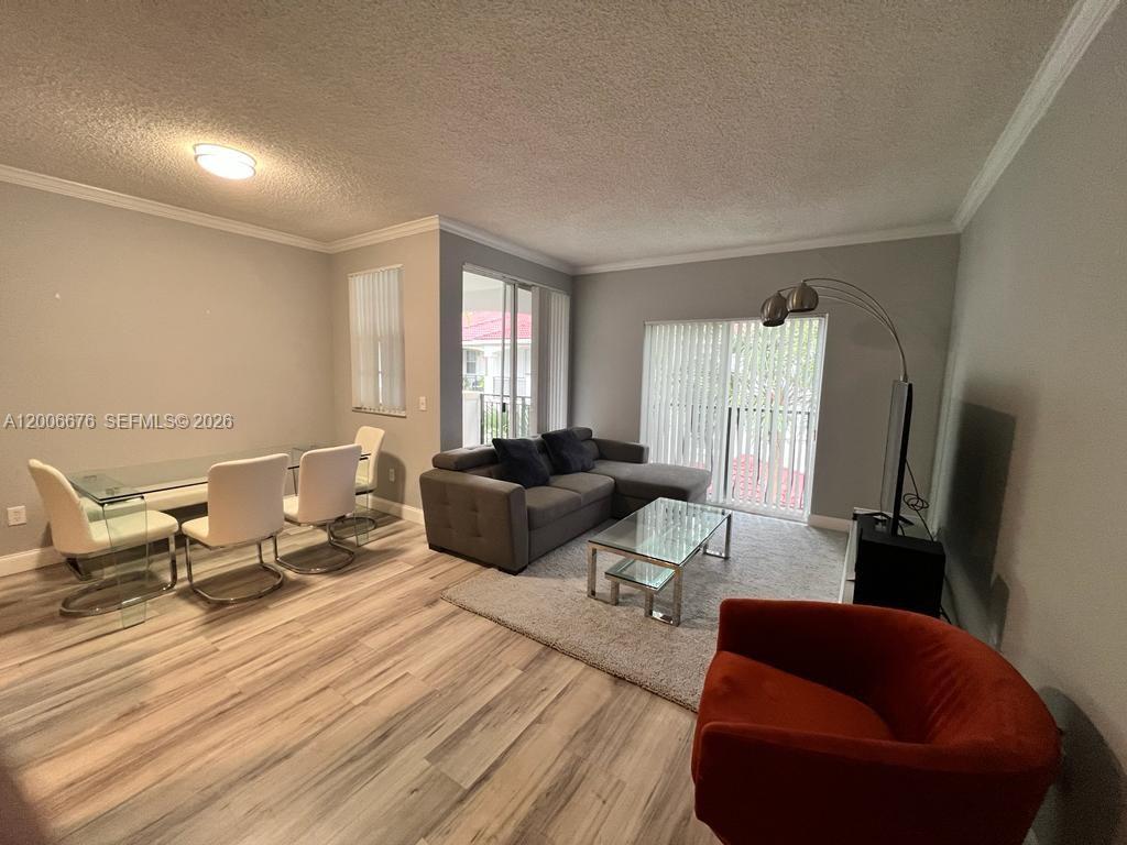 A living and dining area features light wood-look flooring, a gray sectional, and glass tables — AVENTURA, FL