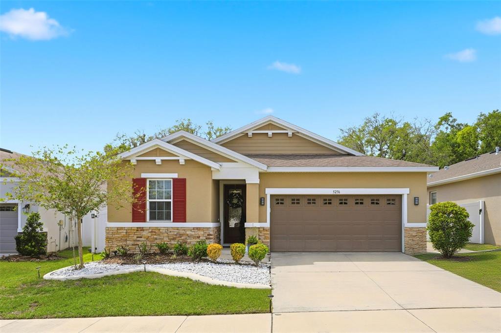 A single-story suburban house with a tan exterior, stone accents, and a two-car garage — 5256 MEADOW SONG DRIVE, OKAHUMPKA, FL