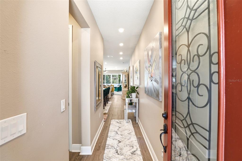 A long entryway with wood-look flooring leads into an open-concept living area — 5256 MEADOW SONG DRIVE, OKAHUMPKA, FL