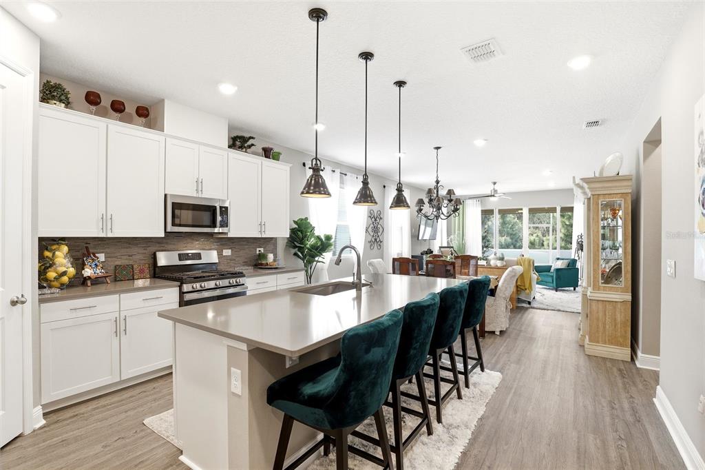 A modern kitchen features white cabinetry, a large gray island with teal stools, and pendant lighting — 5256 MEADOW SONG DRIVE, OKAHUMPKA, FL