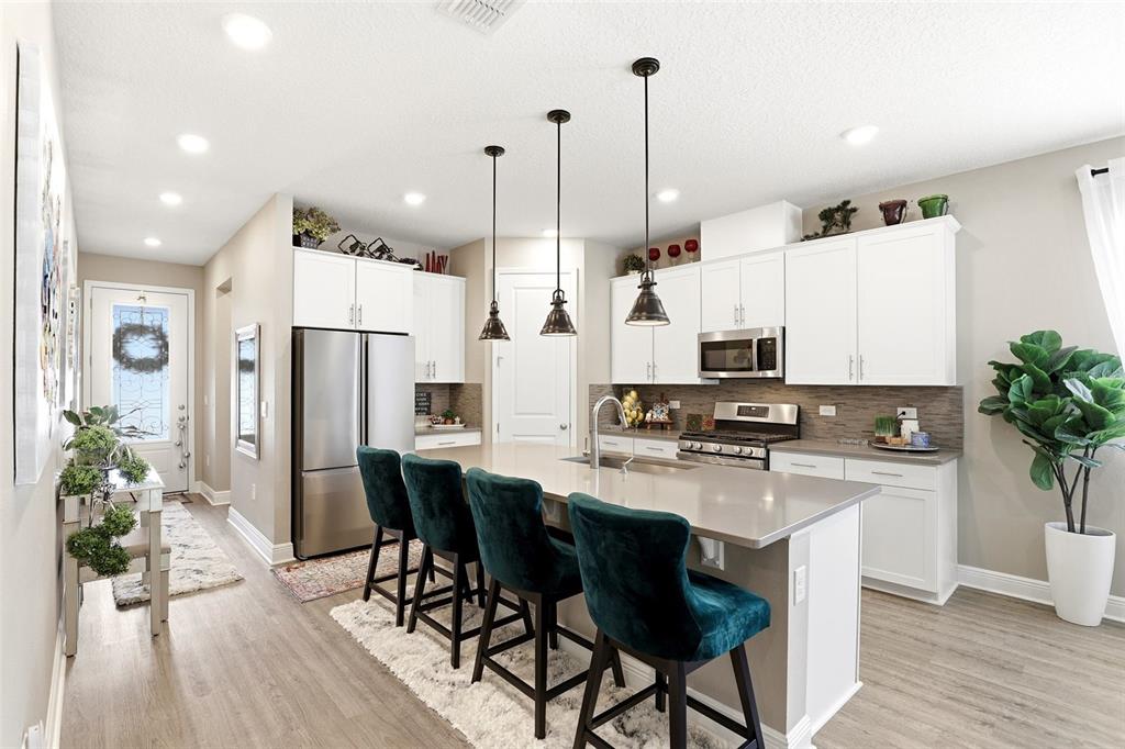 A modern kitchen features white cabinets, a large island with teal stools, and stainless appliances — 5256 MEADOW SONG DRIVE, OKAHUMPKA, FL