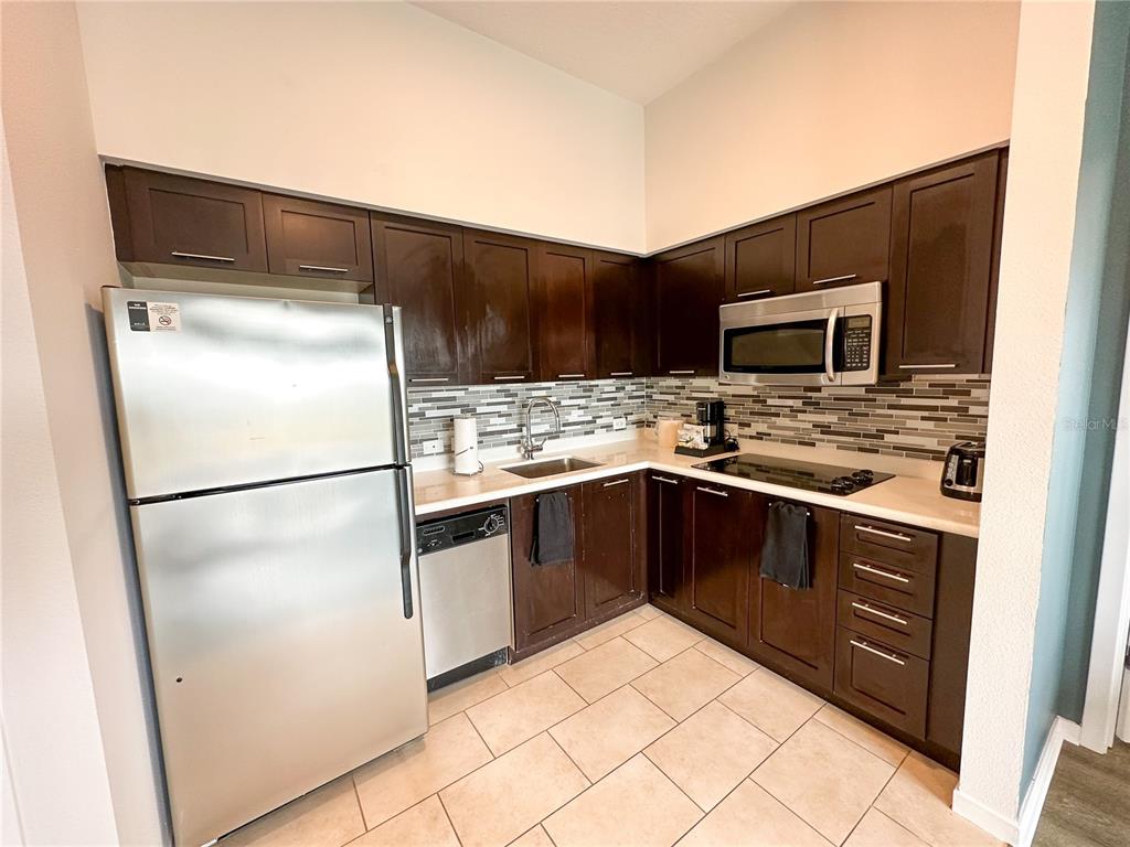 A kitchen features dark wood cabinets, stainless steel appliances, and a tiled backsplash — 225 CELEBRATION PLACE UNIT # 527, KISSIMMEE, FL