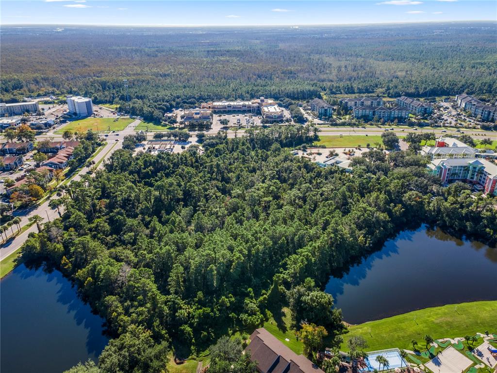 An aerial view shows a wooded lot surrounded by a lake, apartment complexes, and commercial buildings — 11990 INTERNATIONAL DRIVE, ORLANDO, FL